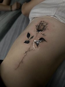 Tatuż przedstawiający realistyczną różę i napisy w delikatnym, kobiecym stylu. Kompozycja umiejscowiona na żebrach, łączy motywy natury i fantastyki w mikrorealistycznym ujęciu.